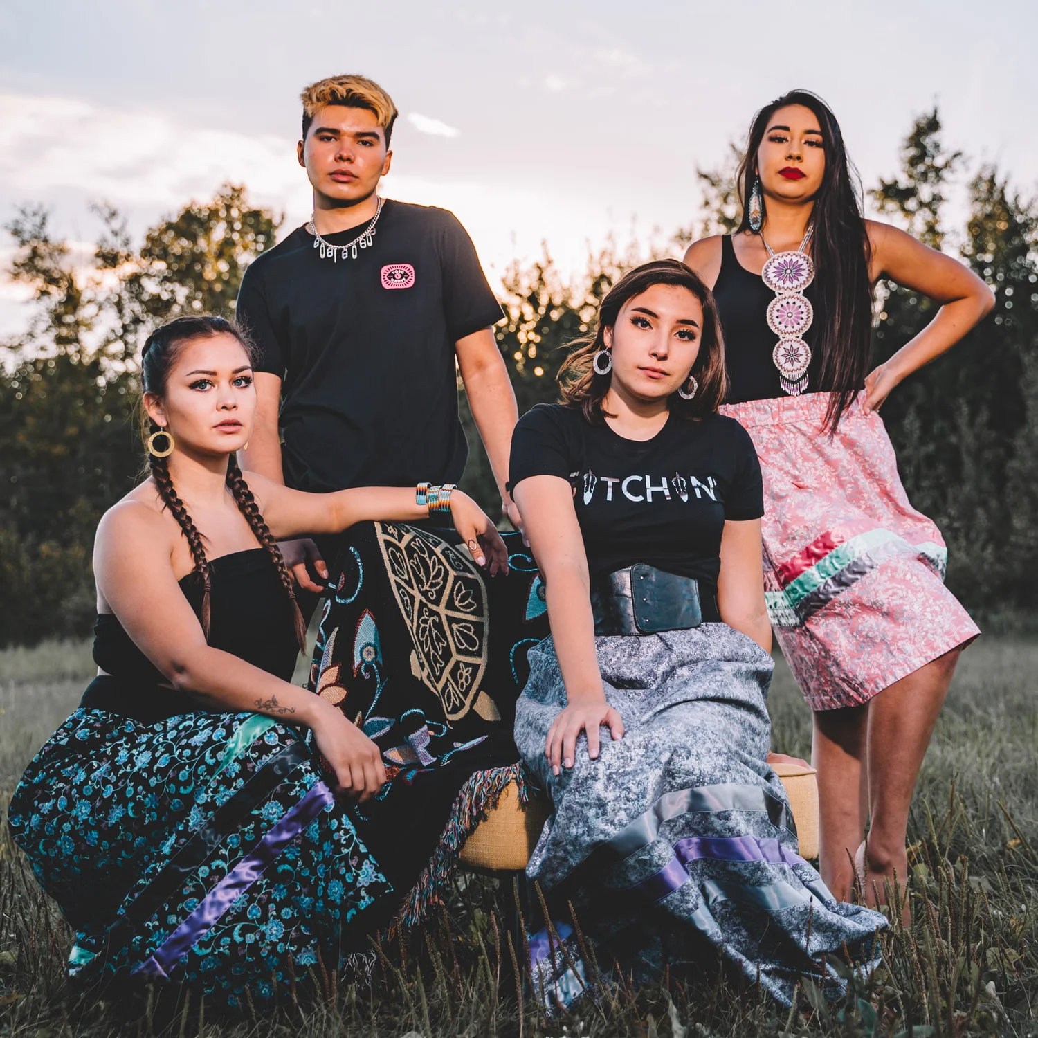 Beyond Buckskin brand image: Four young people sit together in the grass with the sun setting in the background.