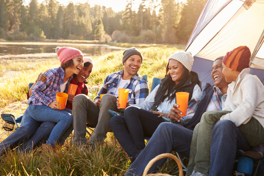 Conscious Gear brand image: Folks gather around in camp chairs by a tent with a lake in the background.