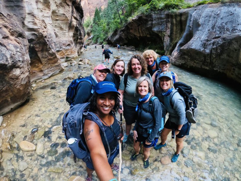 AdventureWomen brand image: Women gather for a selfie in the midst of a gentle river in a canyon.