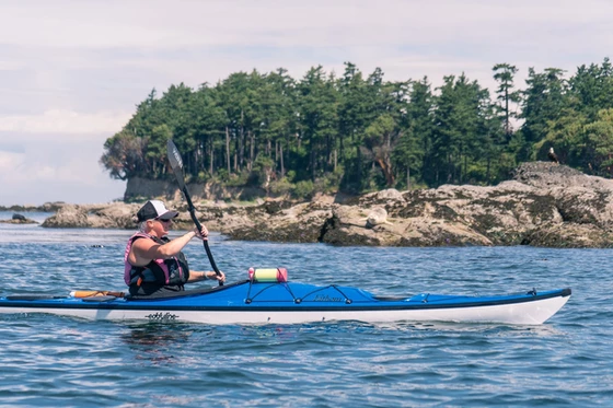 Dragonfly Kayak Tours brand image: A woman paddles in a kayak along the coast of Washington.