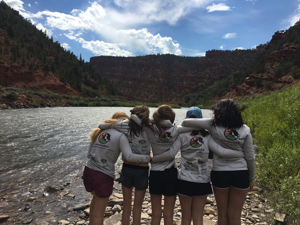 elevateHer brand image: Five young women stand arm-in-arm looking out over a river as it winds through a canyon.