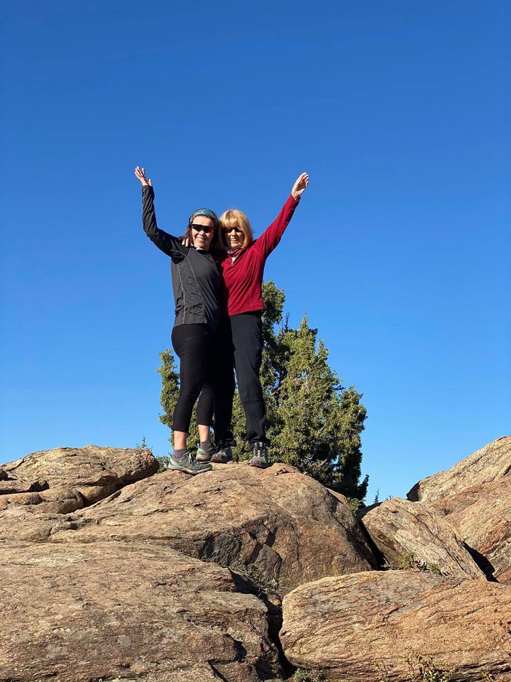 Two women stand atop a rocky outcropping with arms raised in celebration.