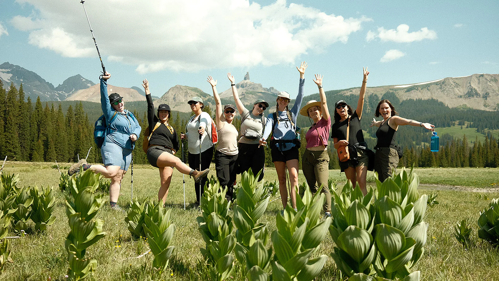 women raise their hands in a field with mountains behind them