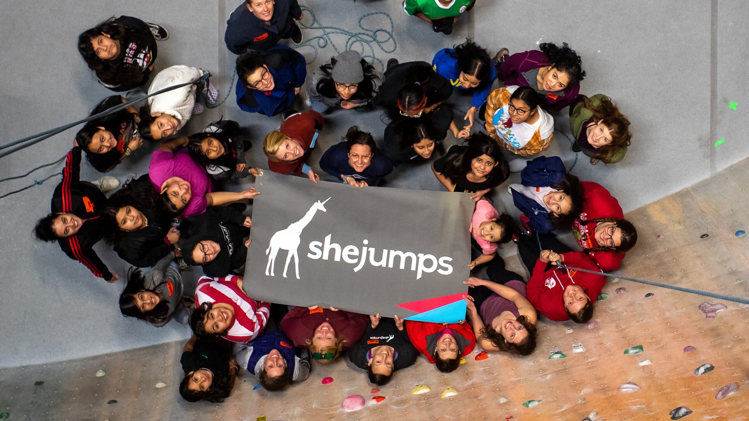a diverse group of women and girls hold a sign that says "shejumps"