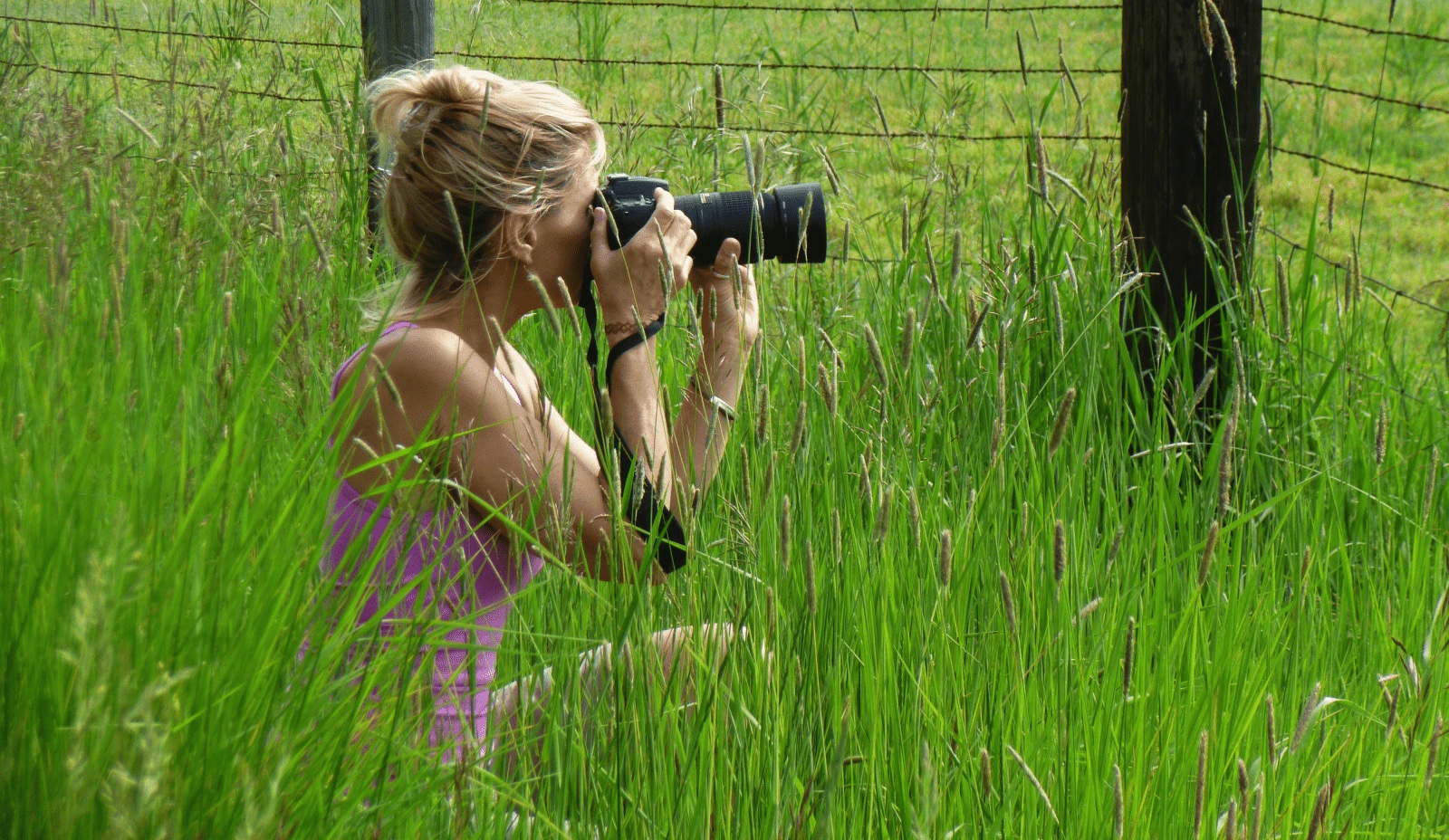 a woman holds a camera to her eye in a grassy field