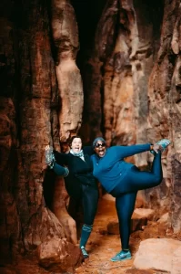 Two women kick up their legs in excitement as they hike beautiful red rock canyons.